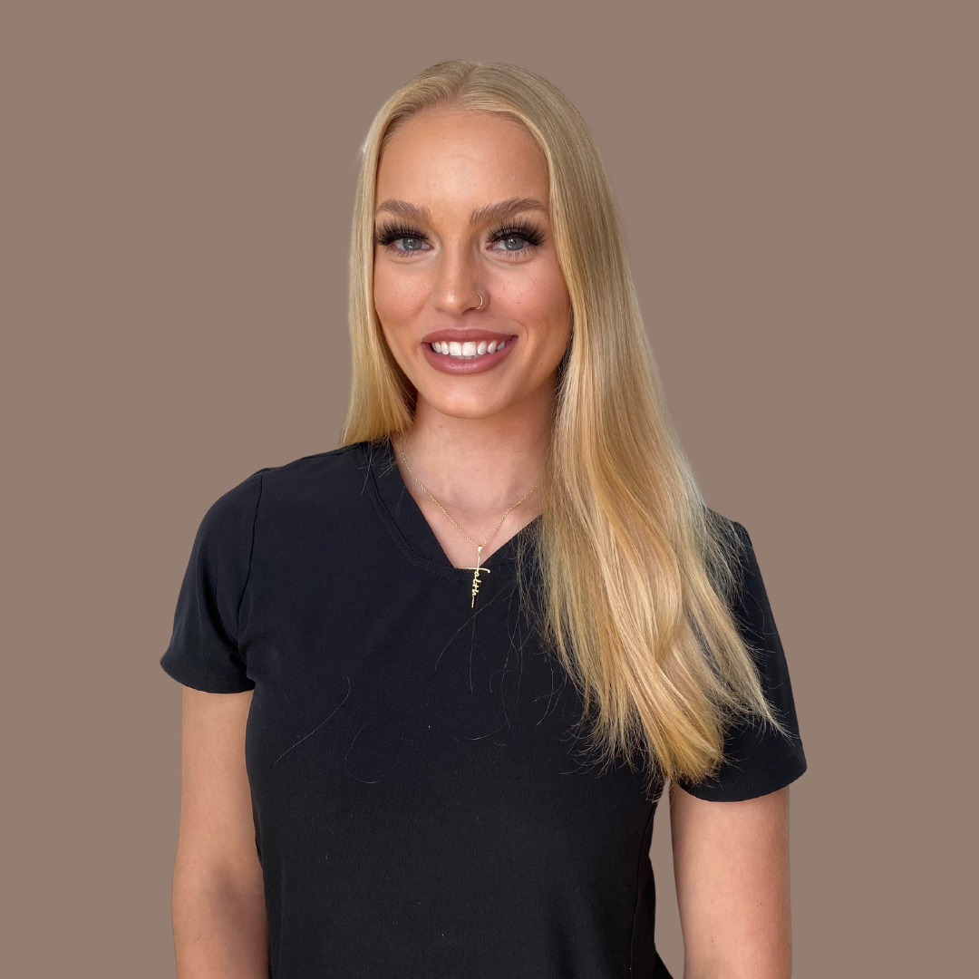 Portrait of a smiling blonde woman in a black T-shirt with a gold necklace, posed against a solid brown background.